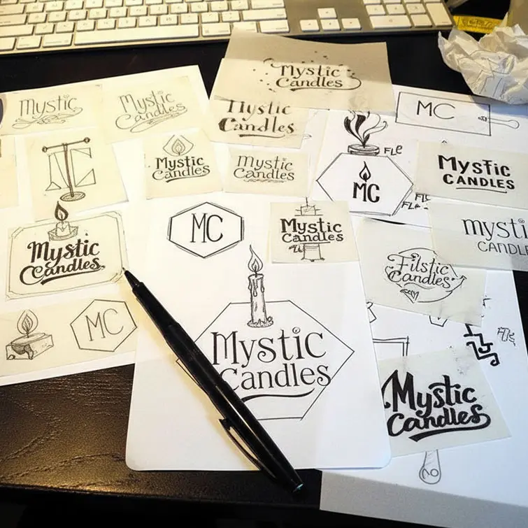 Overhead view of a desk with Mystic Candles logo sketches and a black pen.